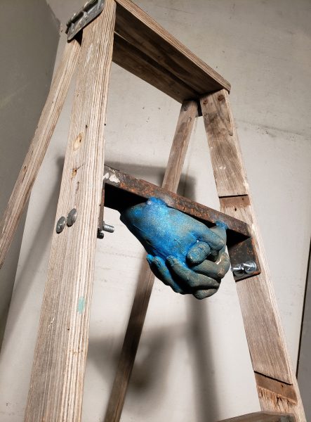 Closeup on blue hand sculptures attached to underside of ladder rungs.
