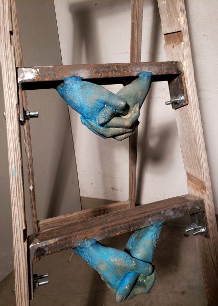 Closeup on blue hand sculptures attached to underside of ladder rungs.