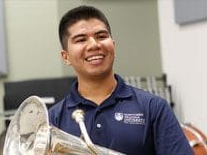 Rueben Miranda holding a brass tuba in a blue N A U polo.