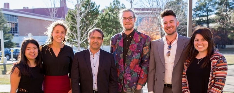 A group of formally dress students and faculty pose for a picture together outside on a sunny day