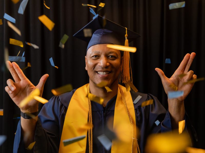An N A U Online graduate poses happily from home in his cap and gown.