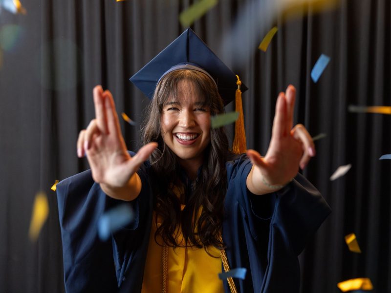 An N A U Online graduate poses joyfully from home in her cap and gown.