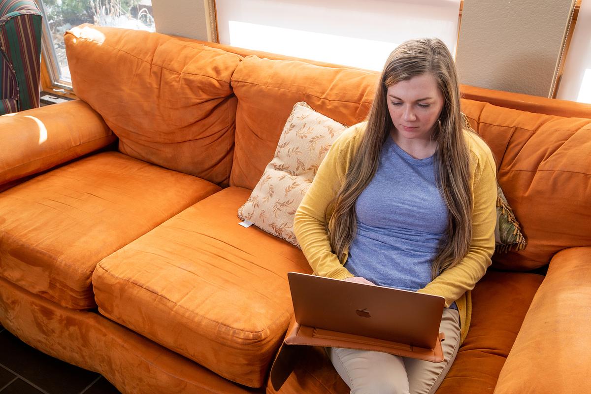 A person sitting on an orange couch, focused on using a laptop computer.