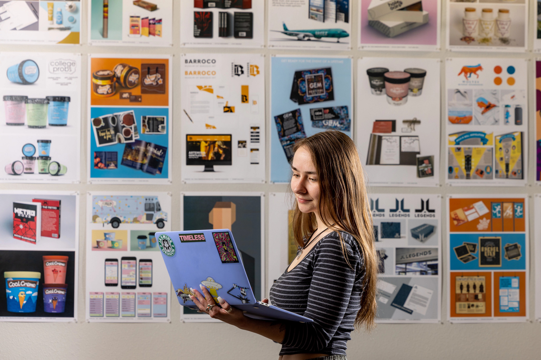 N A U student standing in front of a wall with posters while looking at laptop.