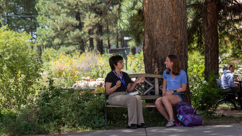 N A U professor and student are sitting on a bench outside talking to each other.