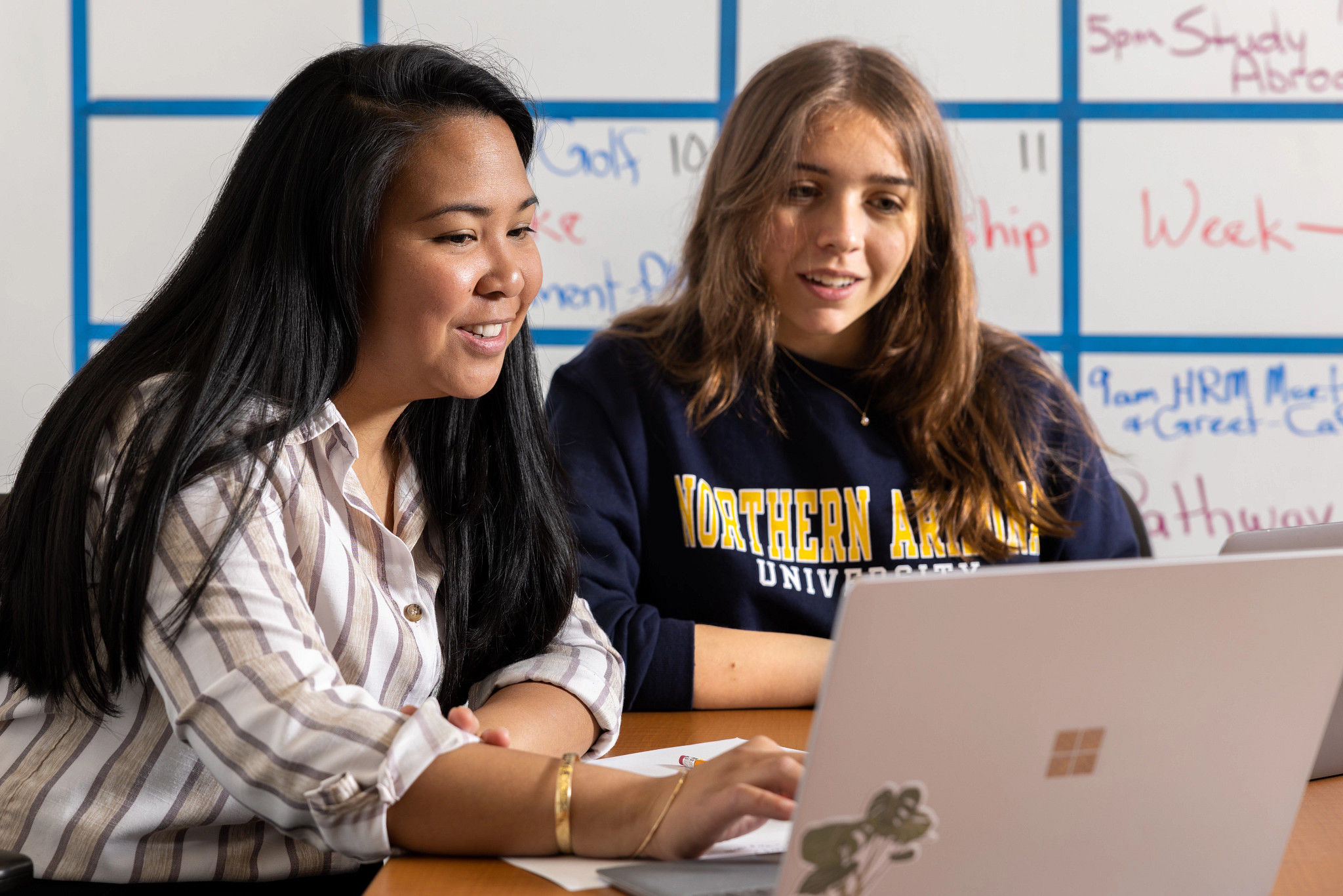 Two N A U students sitting at a table inside working together on a laptop.