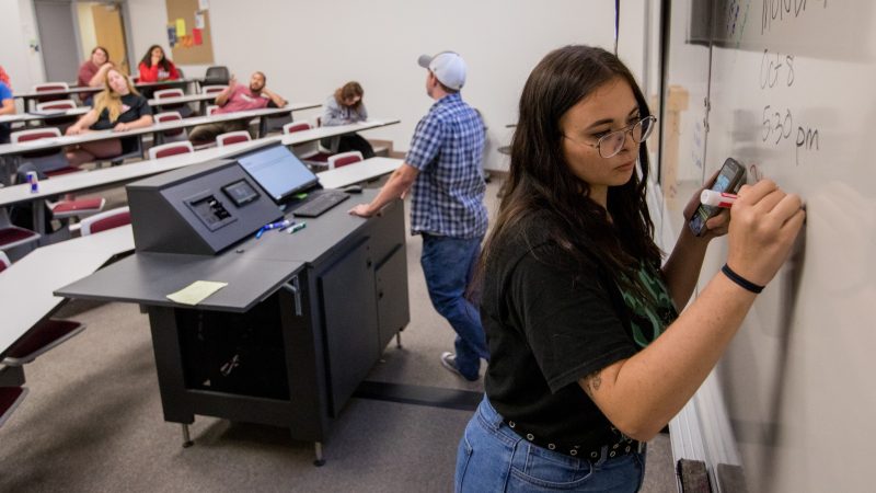 N A U student writing on whiteboard in classroom.