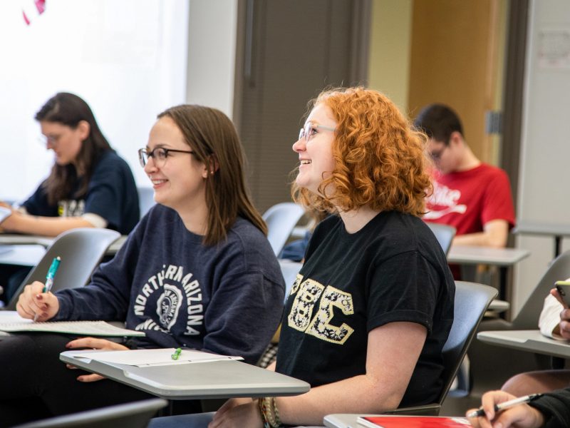 Two students in a classroom smiling off camera.