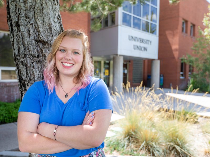 Student smiling and looking at the camera while posing in front of the University Union.