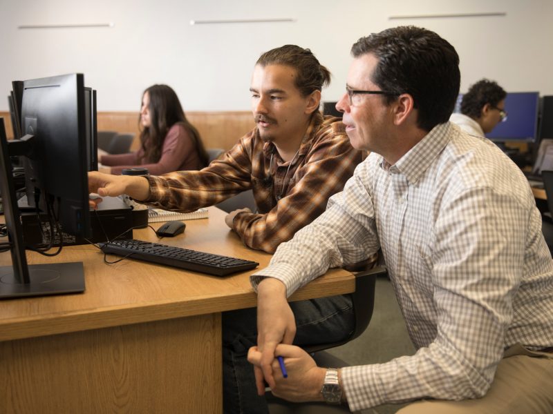 Student being helped by a professor in a computer lab.
