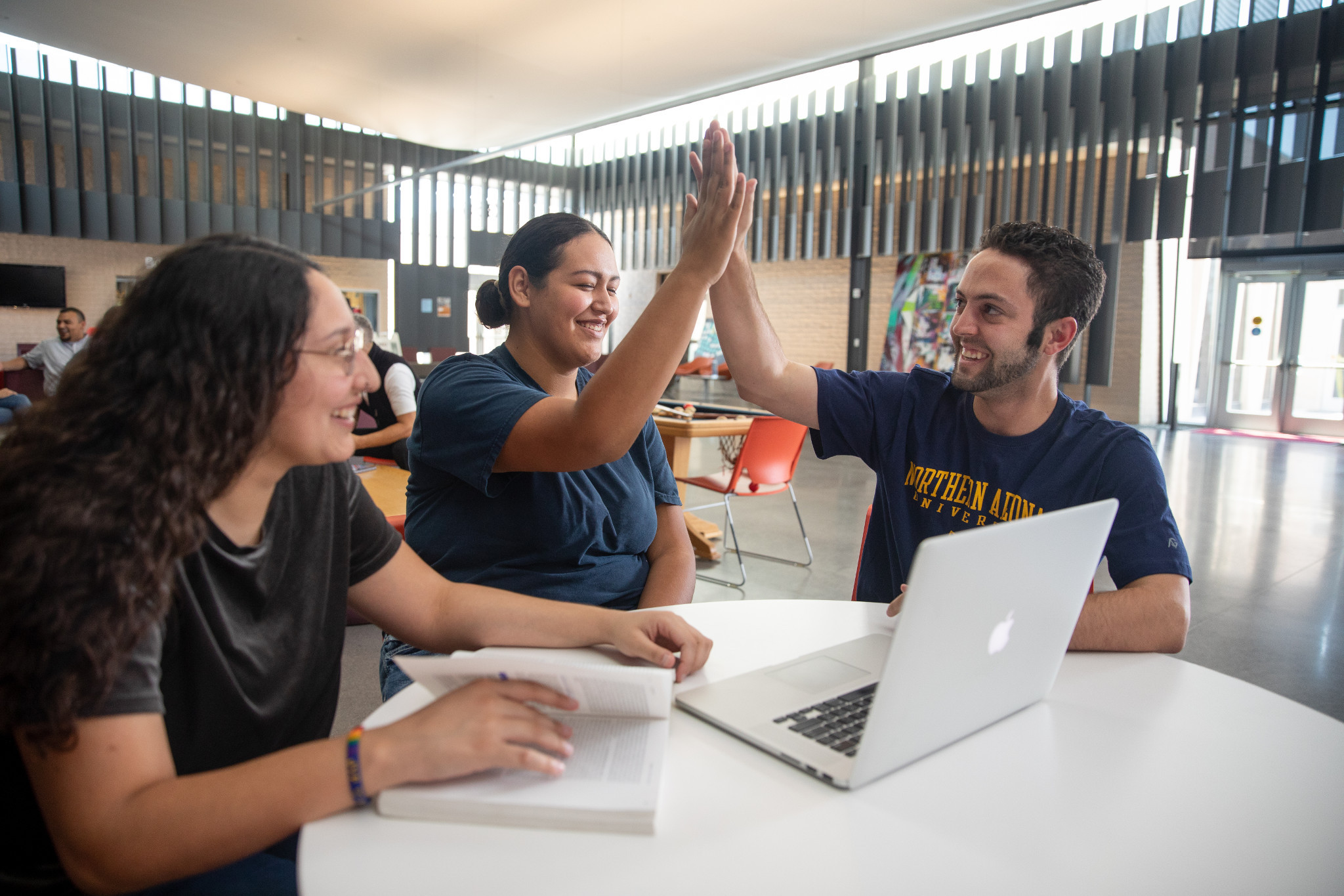 Students high fiving in a lounge while working on a laptop.
