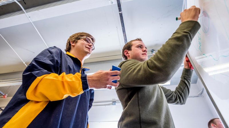 Students working together writing on whiteboard.
