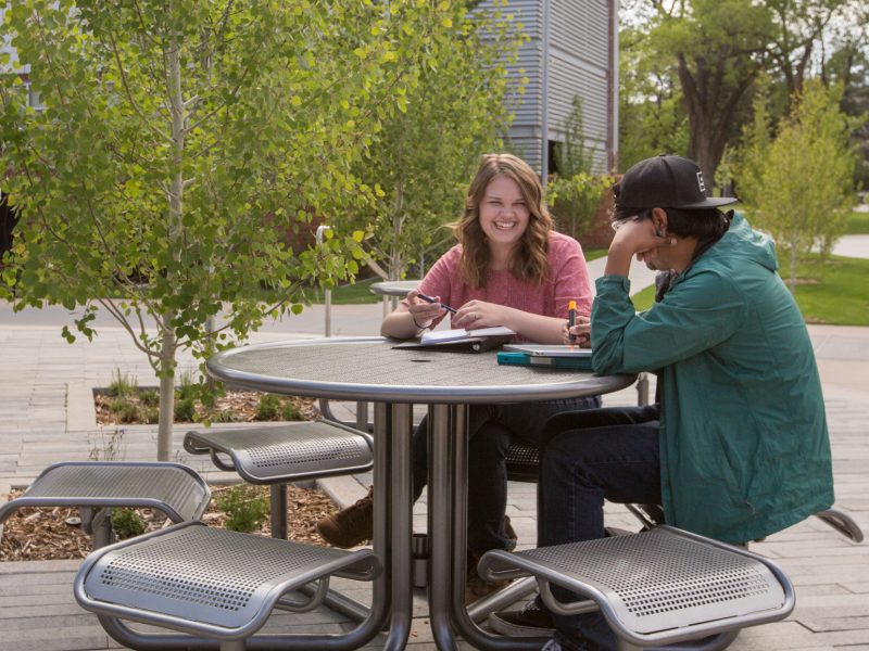 Students smiling and working together in outdoor seating.