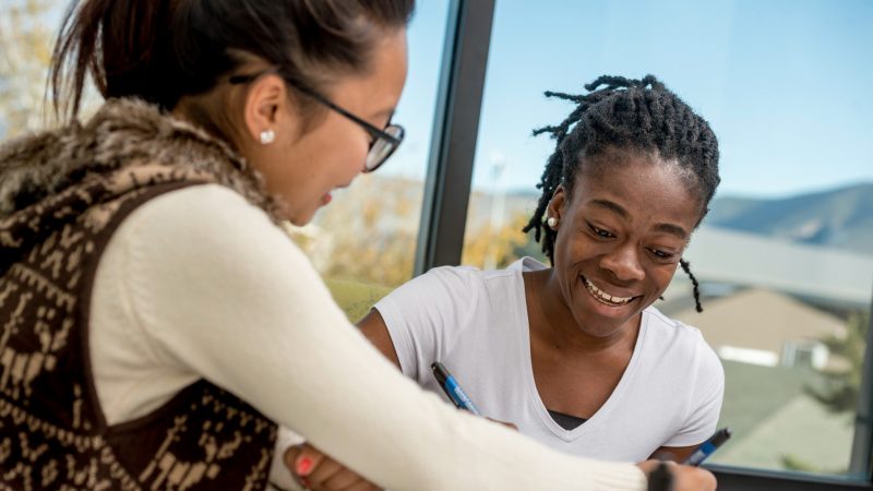 Student and professor smiling working together in a study room with a sky view background.