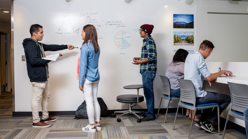 N A U students talking and working at a whiteboard.