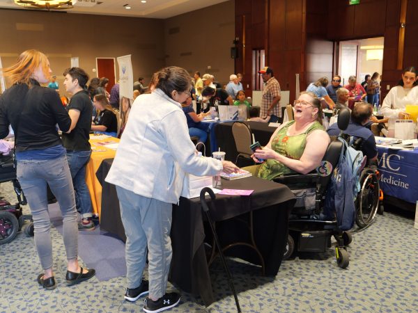 Several people in a exhibit hall setting. One is using a powered wheel chair