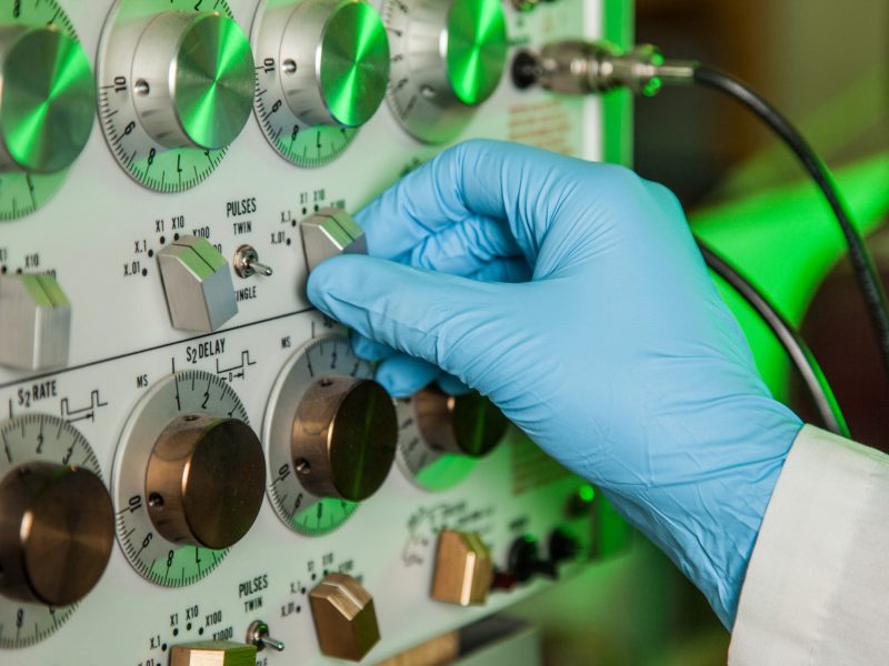 Gloved hand turning dial on equipment with multiple dials.