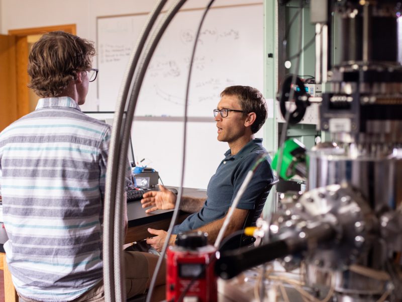 Conversation between two individuals in classroom with metal equipment surrounding.