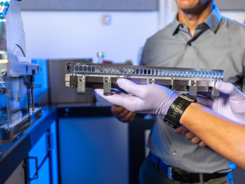 Gloved hands holding metal tray next to metal machine.