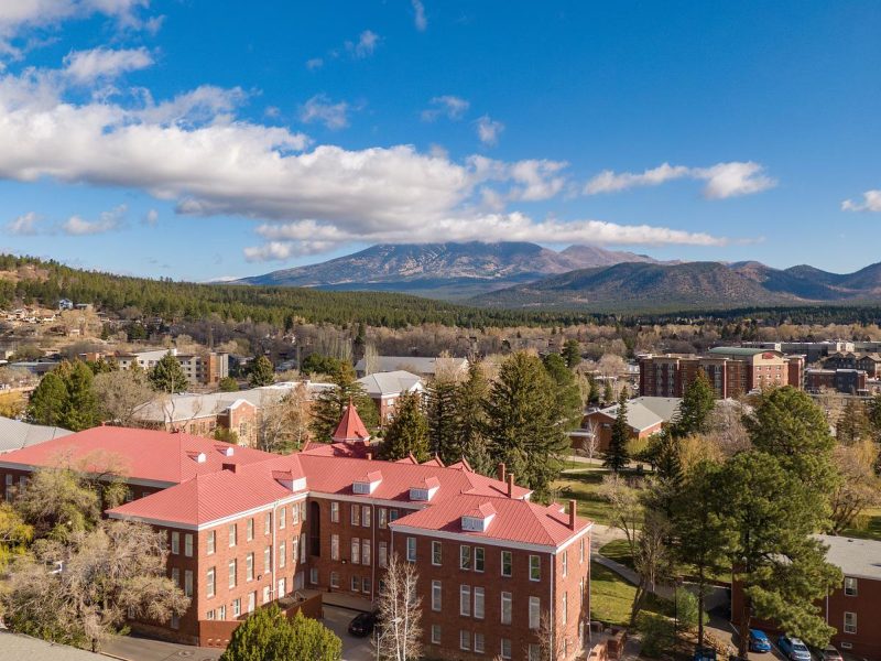 Aerial view of north campus surrounded by mountains, with colorful buildings, trees, and a clear blue sky with wispy clouds.