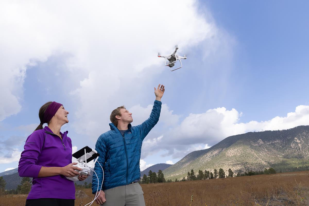 Two N A U researchers in outdoor clothing interacting with a small aerial drone in northern Arizona.