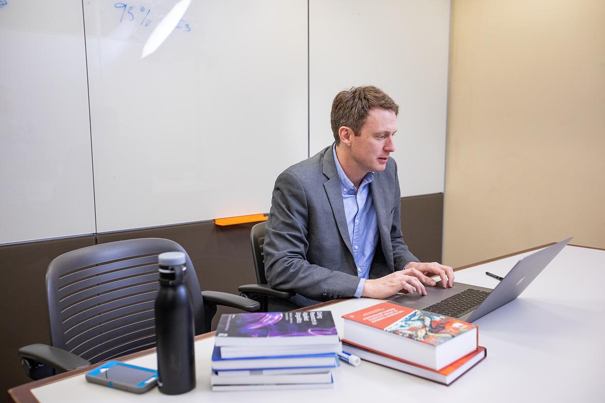 Person sitting at table working on a computer. Several books sit on table.