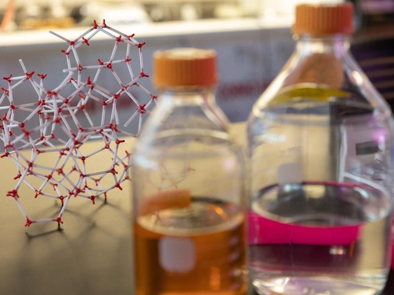 Molecular structure model, bottles of liquid, and laboratory equipment on a surface.