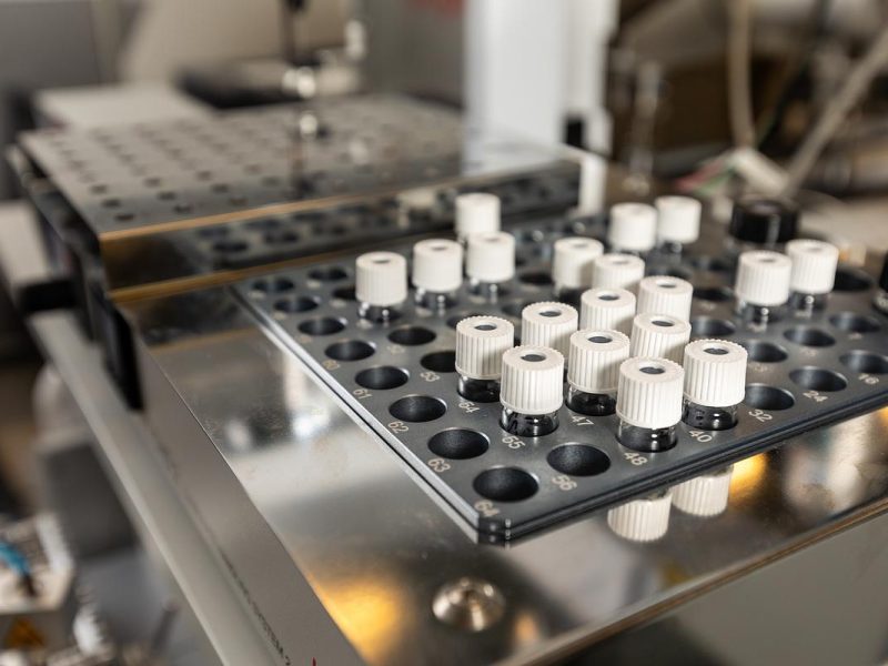 Closeup view of a of vial loaded into a medical instrument with numerous knobs, buttons, and controls on a metal panel.