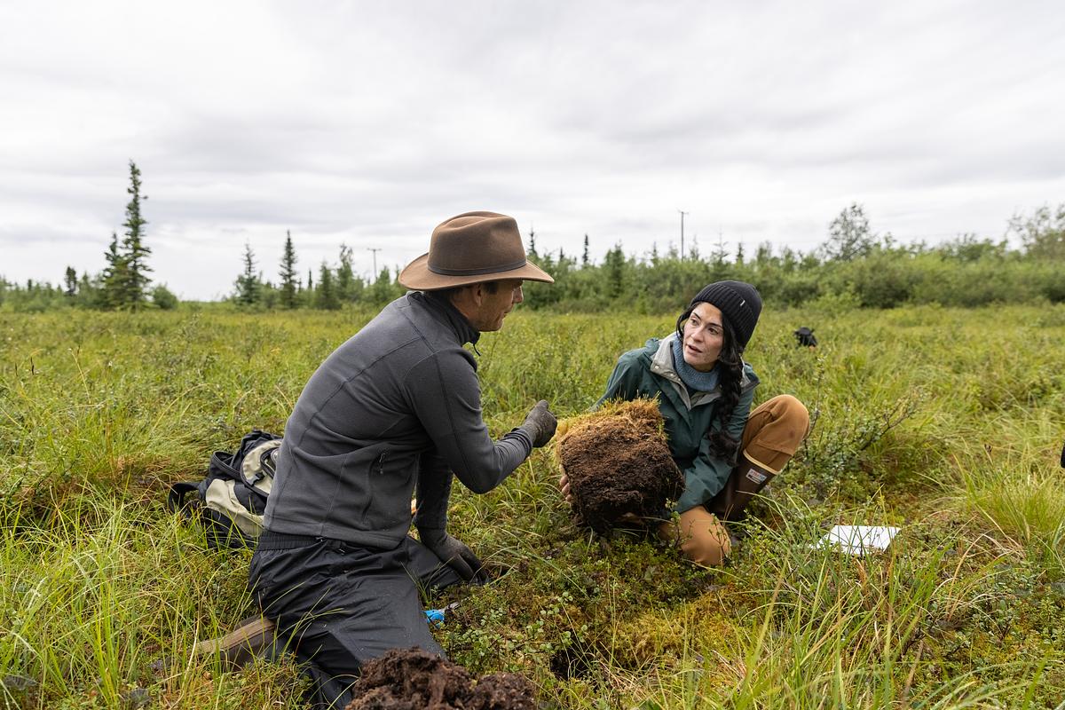 Two researchers working in the Alaskan research field, one wearing a hat and the other wearing a headscarf.