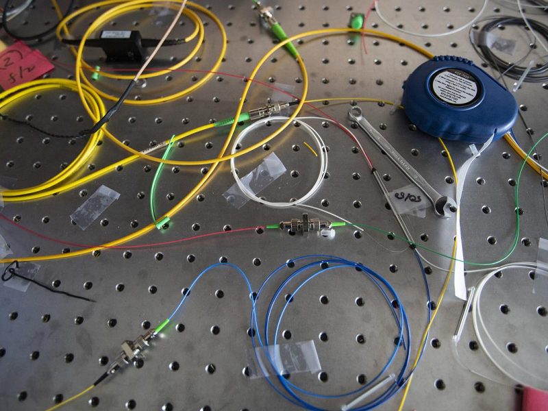 Wires, cables, and electronic components on a perforated board. Various colors of wires and connectors, electronic devices, and a round blue dial or meter visible.