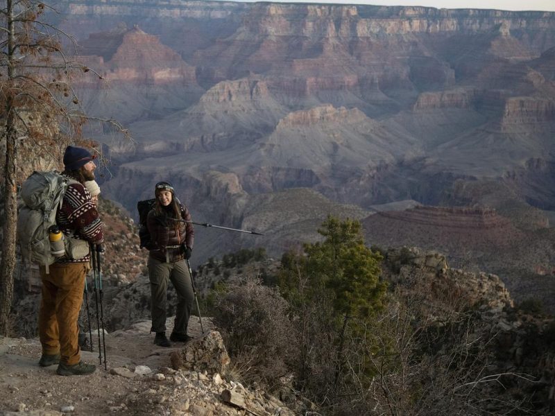 Two researchers standing on a rocky outcrop overlooking the Grand Canyon.