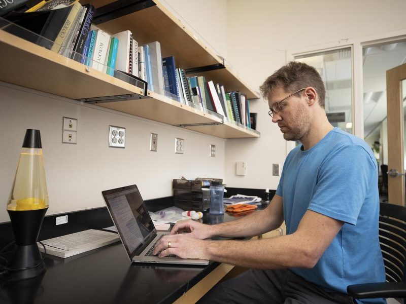 Researcher sitting at a desk entering information on a computer. Appears to be in an office environment.