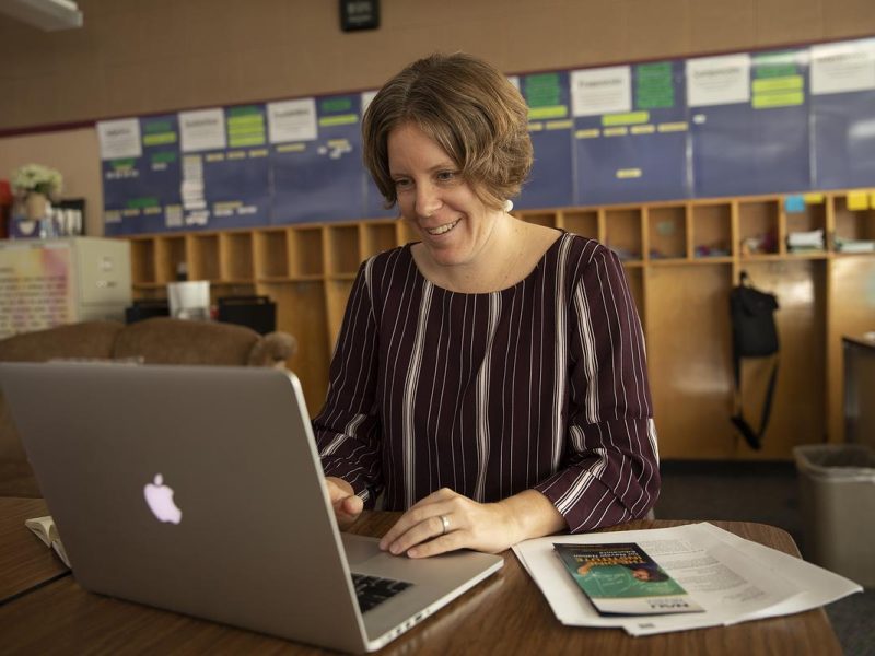 Researcher sitting at a work table entering information into a computer. Appears to be in a classroom environment.