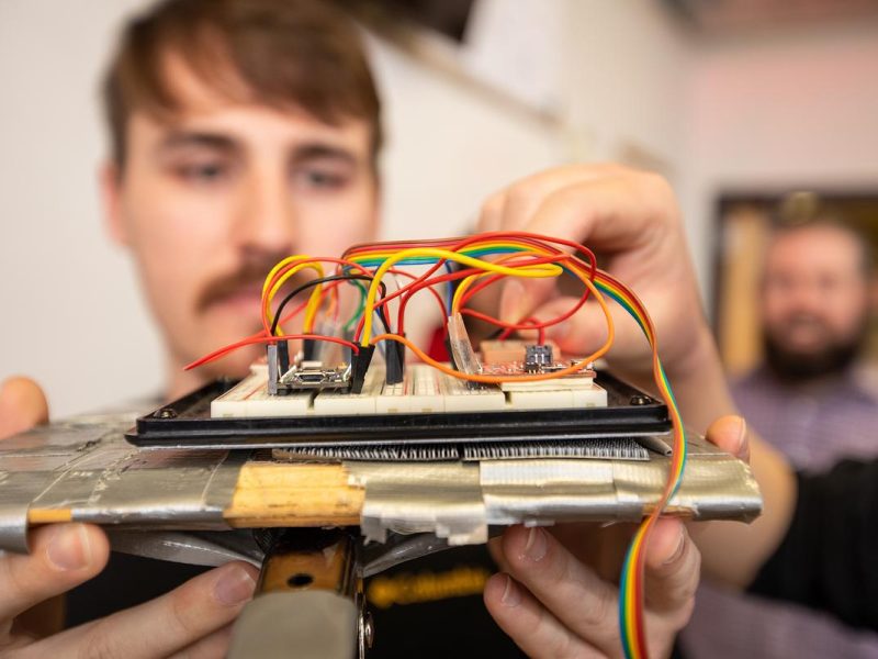A person's hands holding and examining a device with wires and electronic components attached.