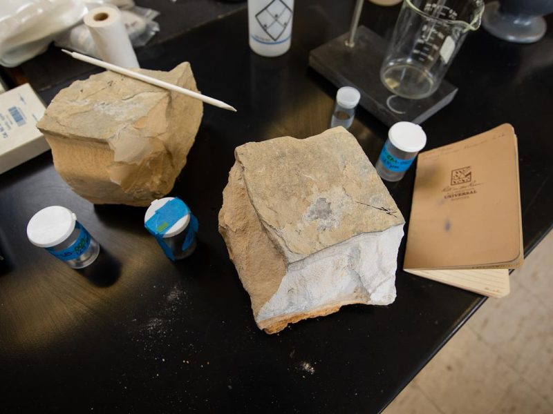 Rocks, bottles, and a notebook on a dark surface in a research lab.