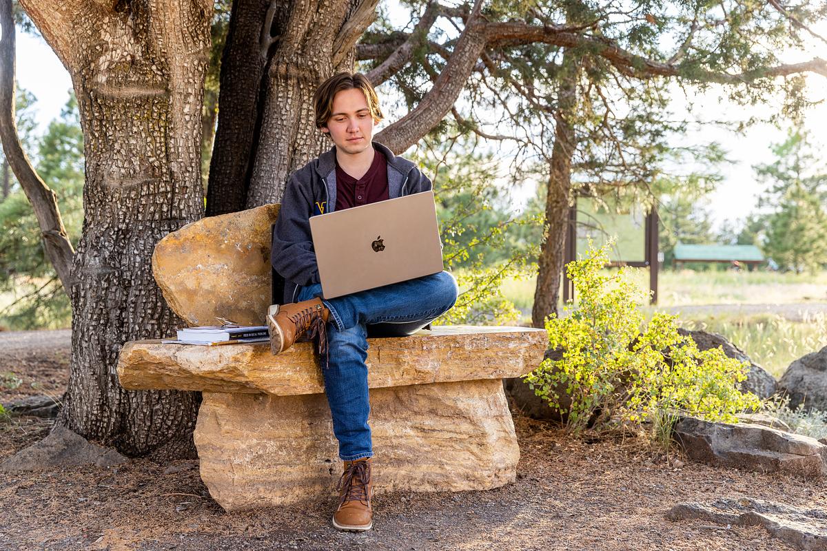 Person sitting on a bench outdoors in nature with pine trees.