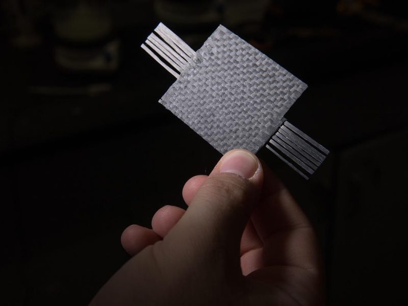 Hand holding a black capacitor with geometric pattern and black stripes.