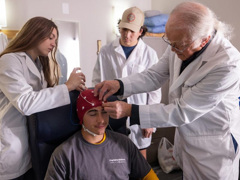 People wearing white labs coats placing brain scan device on a patients head.