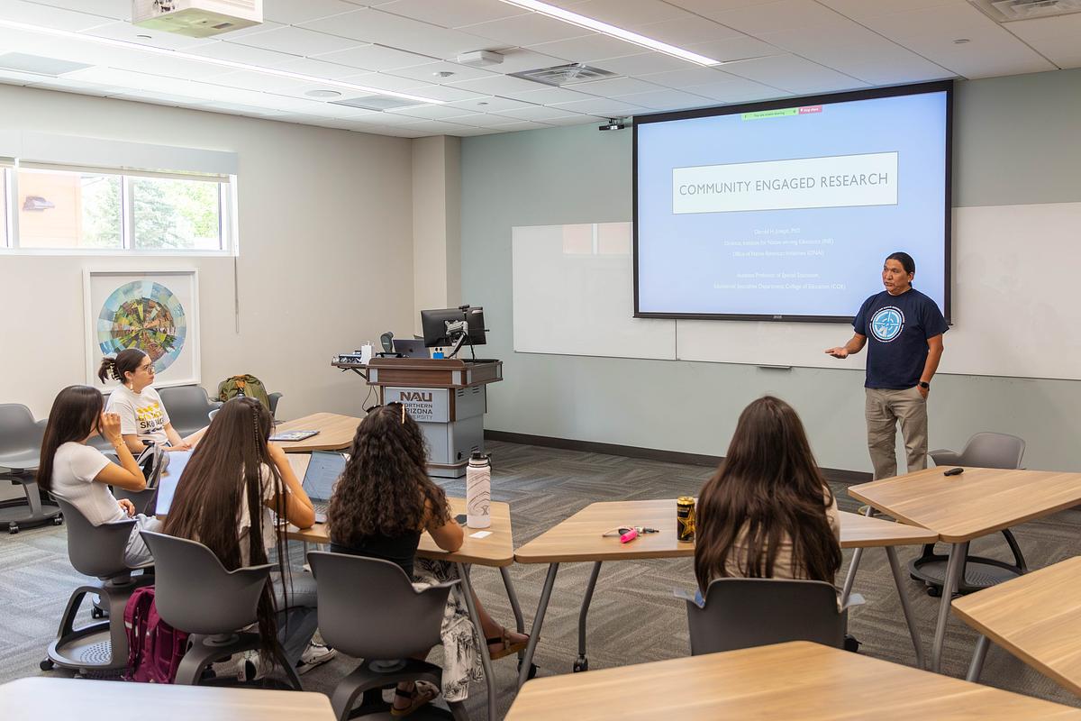 Person standing in front of several other people discussing community engaged research in a classroom.