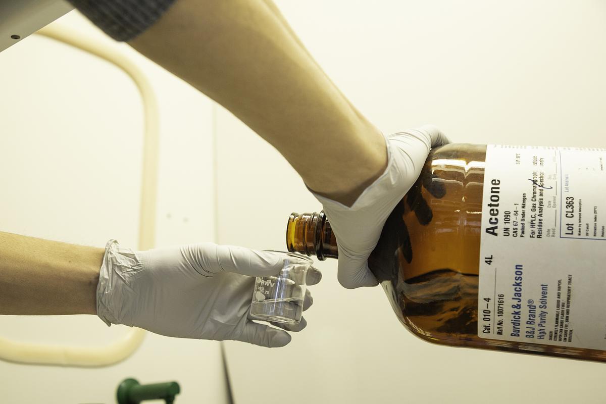 Person pouring a bottle filled with acetone into a beaker.