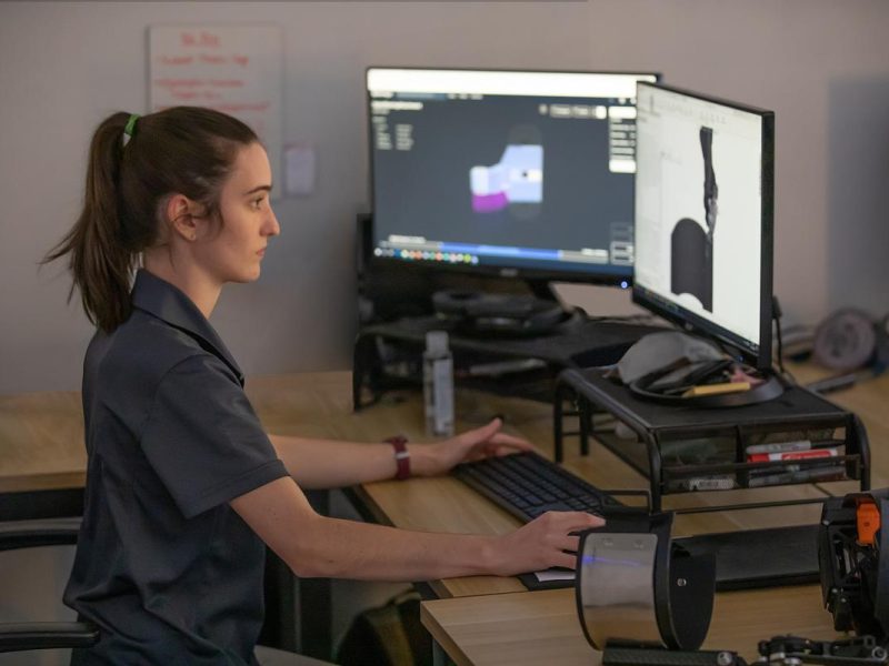 Person working on computer with two screens. It is in a classroom environment.