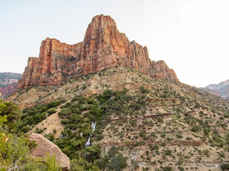Red rock formation with green bushes and a waterfall at the Grand Canyon.