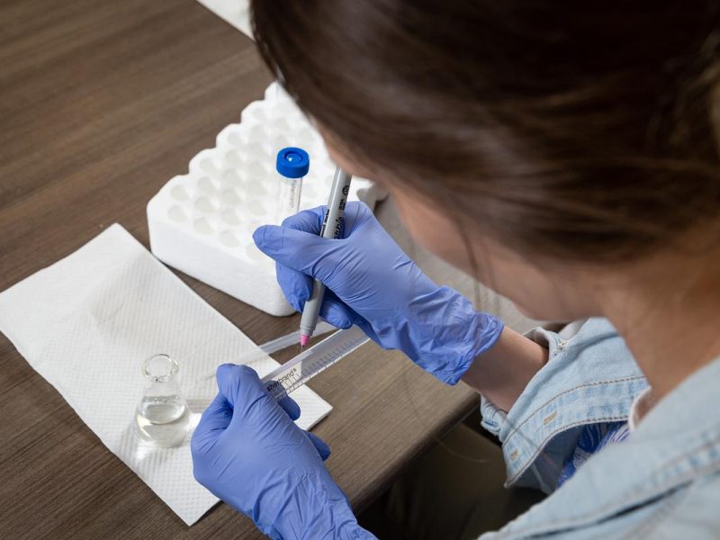 Person wearing a white lab coat and purple gloves writing on a sample.