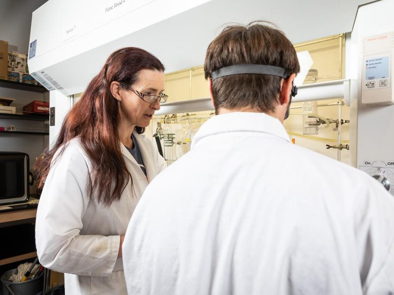 Two people wearing white labs coats working in a lab.