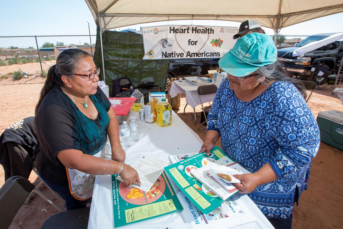 One woman showing another woman the benefits of heart healthy foods. They are outside at an expo.