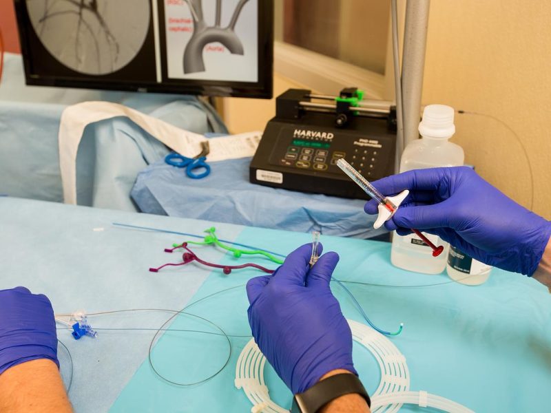 A person wearing purple gloves using medical equipment with a computer in the background.