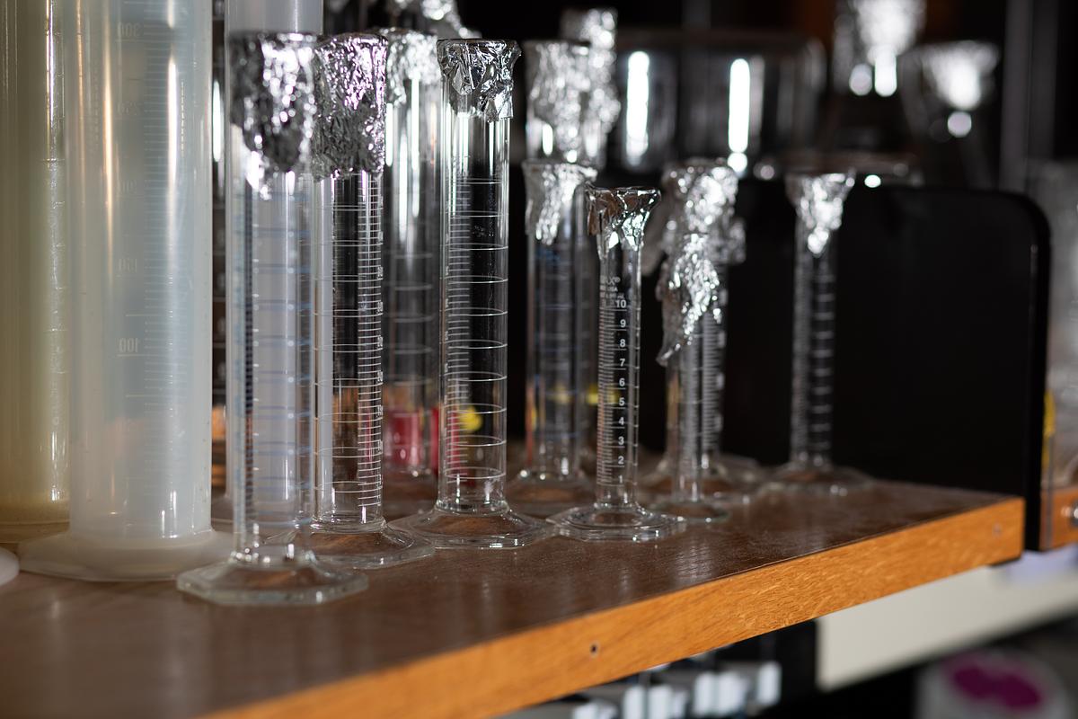 Group of glass containers with measurements written on them sitting on a wood desk.
