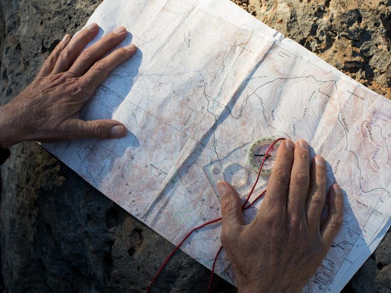 Map and compass laying on a rock with hands holding the items.