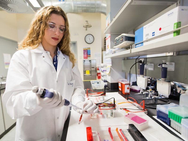 Student wearing a white lab coat working on pipetting samples in a lab.
