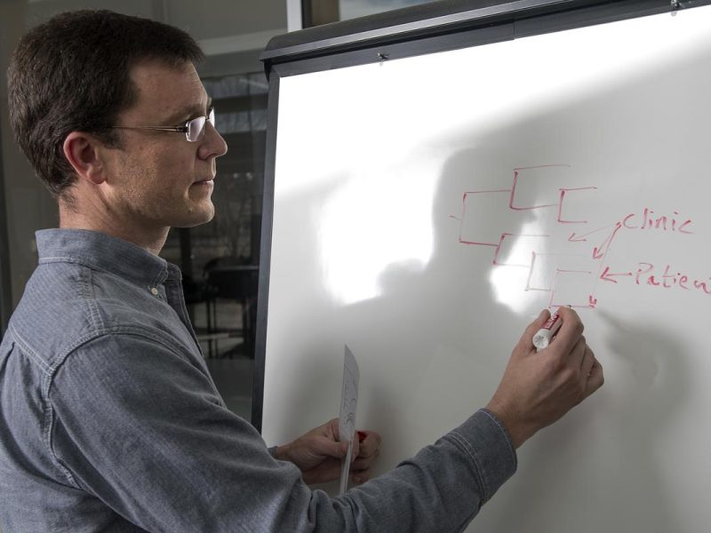 Person wearing a blue shirt standing in front of a white board with text that says clinic and patient.